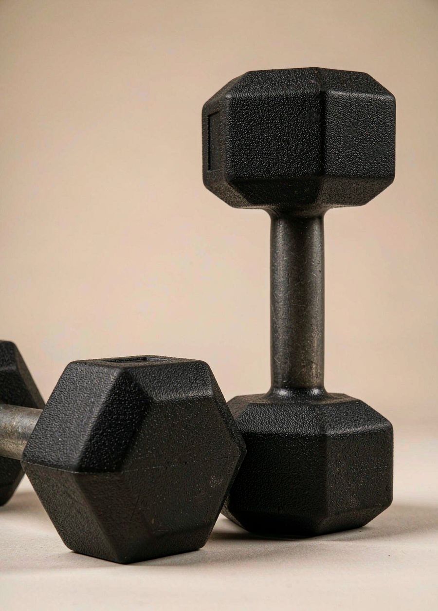 A pair of black rubber hex dumbbells with steel handles on a warm bone background.